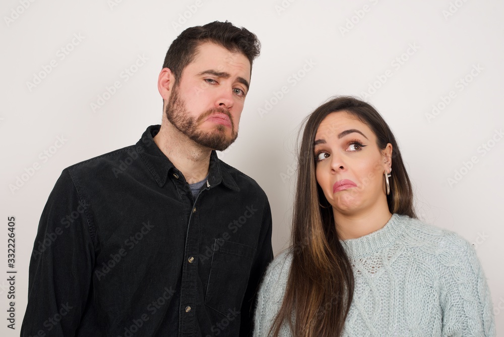 Beautiful couple with snobbish expression curving lips and raising eyebrows, looking with doubtful and skeptical expression, suspect and doubt. Standing indoors over gray background. Beautiful couple with snobbish expression curving lips and raising eyebrows, looking with doubtful and skeptical expression, suspect and doubt. Standing indoors over gray background.