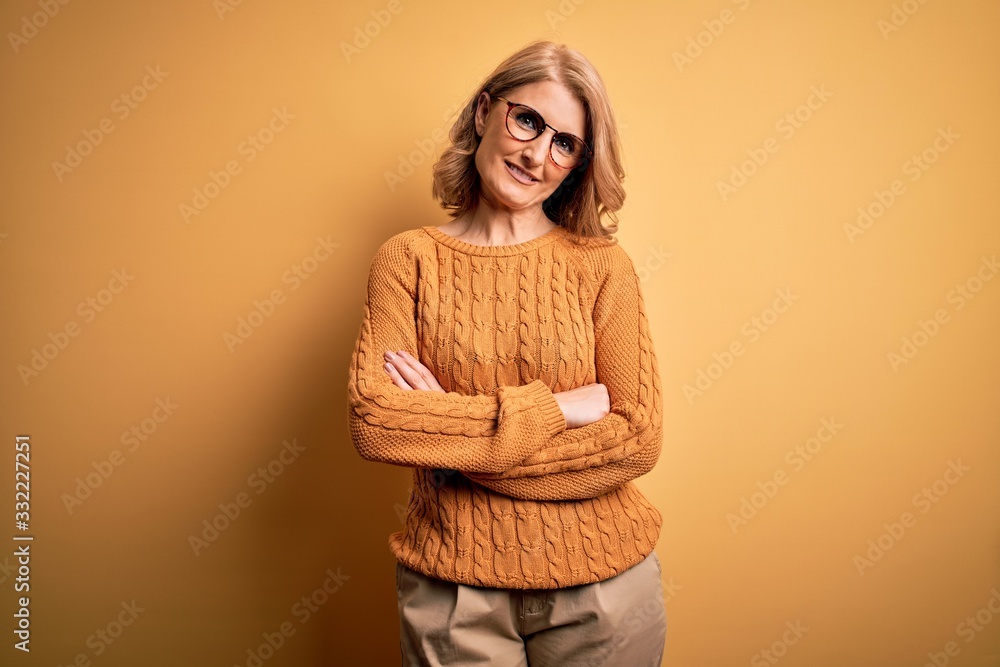 Middle age beautiful blonde woman wearing casual sweater and glasses over yellow background happy face smiling with crossed arms looking at the camera. Positive person. Middle age beautiful blonde woman wearing casual sweater and glasses over yellow background happy face smiling with crossed arms looking at the camera. Positive person.