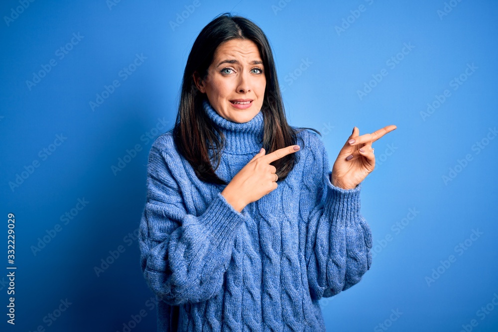 Young brunette woman with blue eyes wearing casual turtleneck sweater Pointing aside worried and nervous with both hands, concerned and surprised expression Young brunette woman with blue eyes wearing casual turtleneck sweater Pointing aside worried and nervous with both hands, concerned and surprised expression
