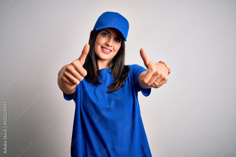 Young delivery woman with blue eyes wearing cap standing over blue background approving doing positive gesture with hand, thumbs up smiling and happy for success. Winner gesture. Young delivery woman with blue eyes wearing cap standing over blue background approving doing positive gesture with hand, thumbs up smiling and happy for success. Winner gesture.