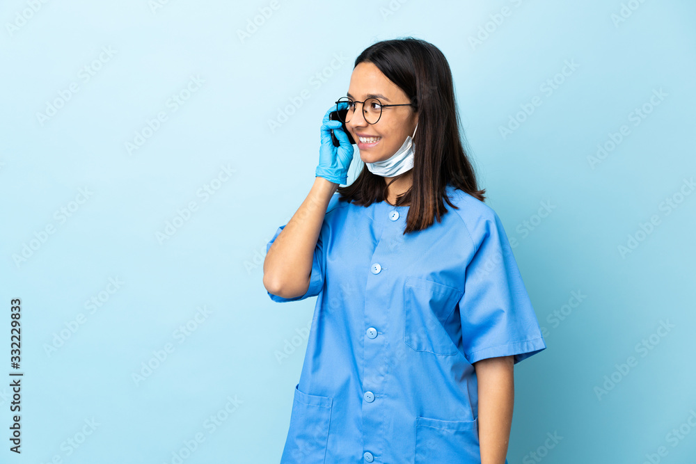 Surgeon woman over isolated blue background keeping a conversation with the mobile phone Surgeon woman over isolated blue background keeping a conversation with the mobile phone