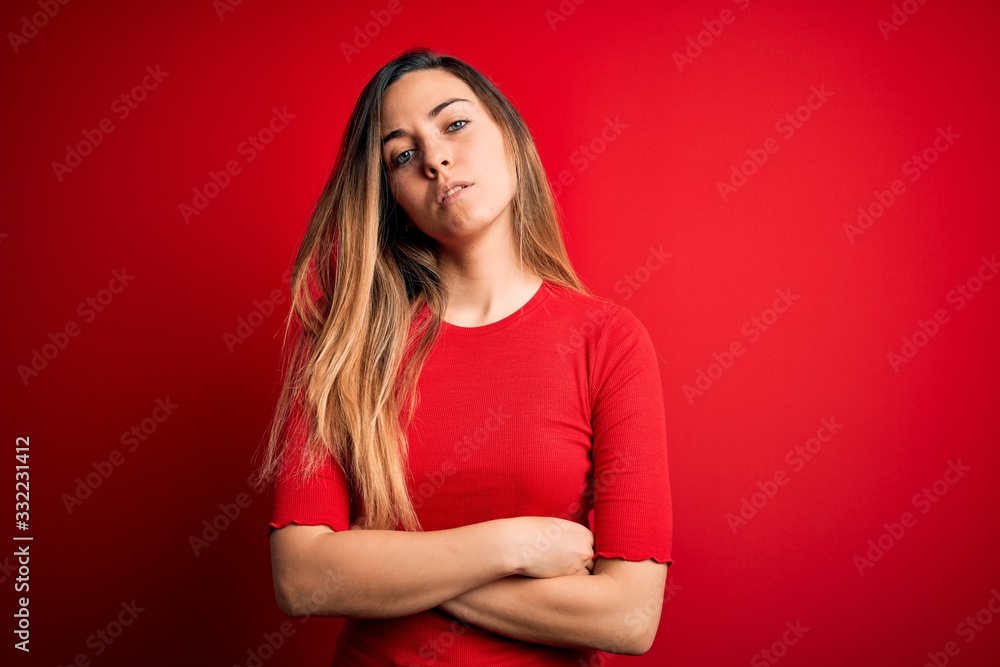 Young beautiful blonde woman with blue eyes wearing casual t-shirt over red background Relaxed with serious expression on face. Simple and natural looking at the camera. Young beautiful blonde woman with blue eyes wearing casual t-shirt over red background Relaxed with serious expression on face. Simple and natural looking at the camera.