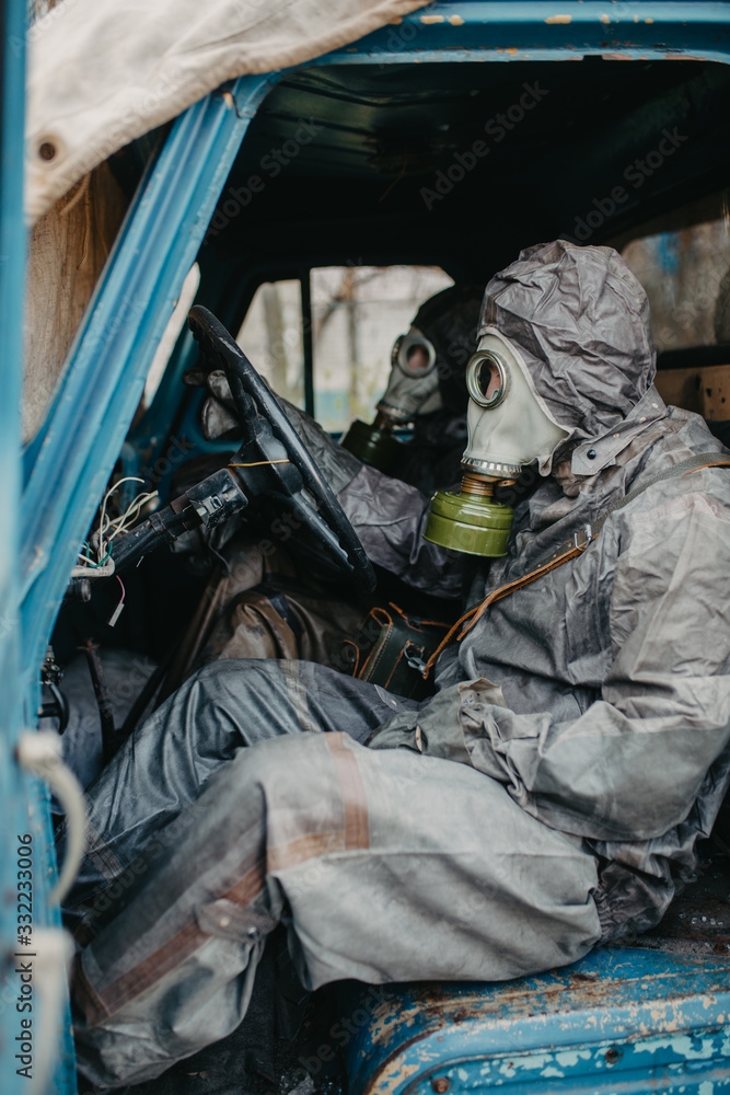 Two persons sits in NBC protective suits and gas masks in old truck. Two persons sits in NBC protective suits and gas masks in old truck.