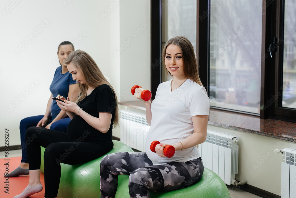 Obraz premium A group of young pregnant mothers are engaged in Pilates and ball sports at a fitness club. Pregnant