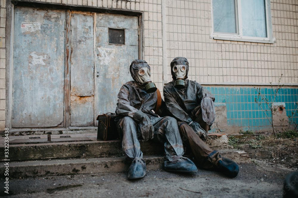 Fototapeta premium Couple in love sits in NBC protective suits and gas masks near building.