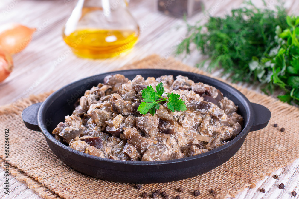 Stewed eggplant with vegetables and sour cream in a pan on a wooden table Stewed eggplant with vegetables and sour cream in a pan on a wooden table
