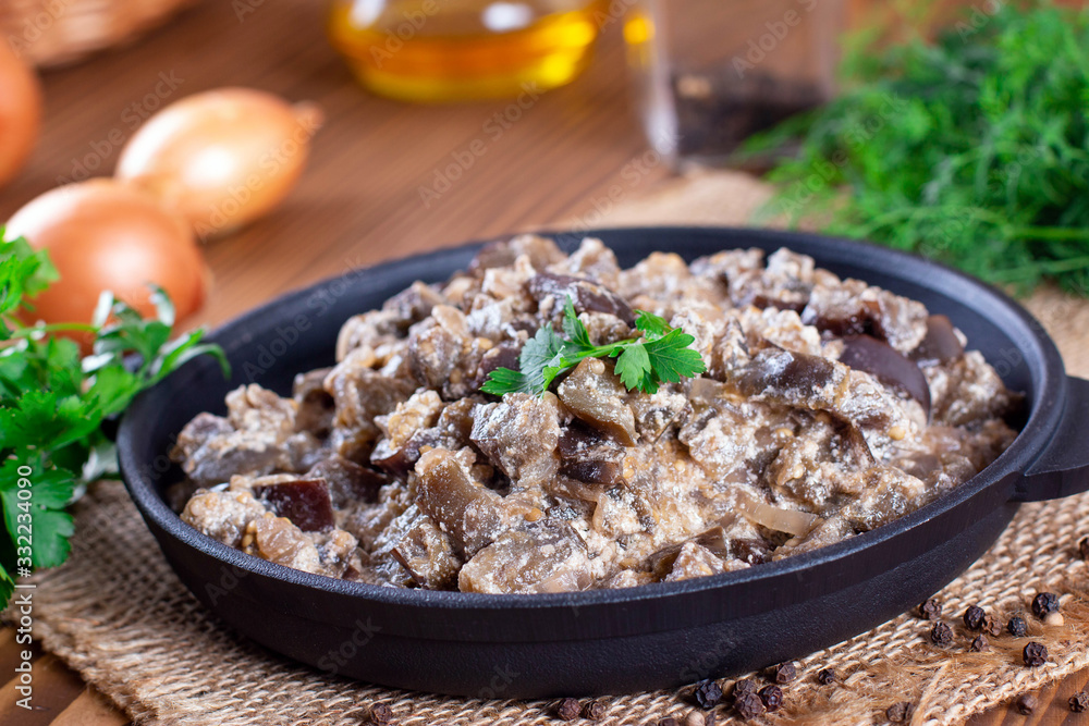 Stewed eggplant with vegetables and sour cream in a pan on a wooden table Stewed eggplant with vegetables and sour cream in a pan on a wooden table
