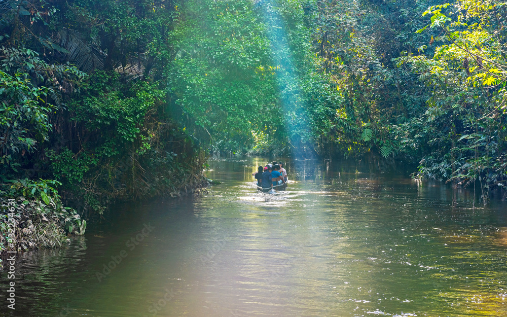 People in a canoe along a canal in the Amazon Rainforest with sunbeam, Yasuni national park, Ecuador. People in a canoe along a canal in the Amazon Rainforest with sunbeam, Yasuni national park, Ecuador.