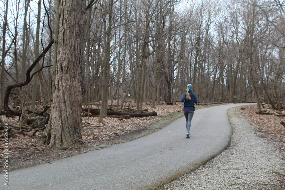 Woman with a long blonde pony tail running on the North Branch Trail in Morton Grove, Illinois with winter clothes