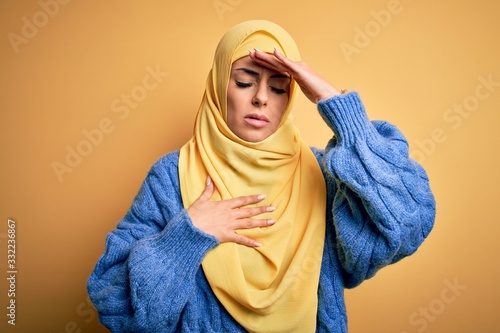Young beautiful brunette muslim woman wearing arab hijab over isolated yellow background Touching forehead for illness and fever, flu and cold, virus sick © Krakenimages.com