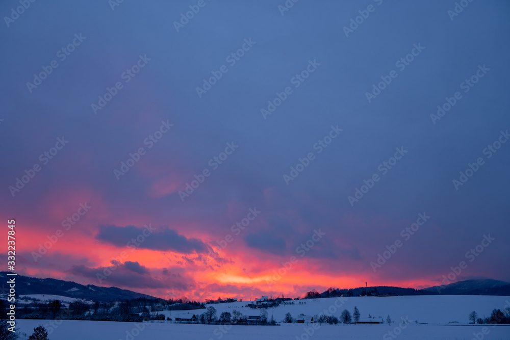 Red clouds at sunrise in winter in the mountains with several houses in the valley Red clouds at sunrise in winter in the mountains with several houses in the valley