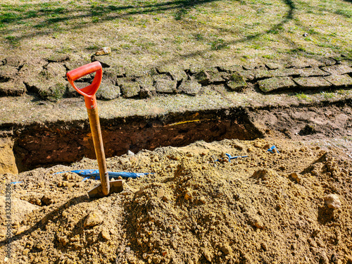 Old earth showel next to deep trench in progress at underground pipe install home garden site during sunny spring day