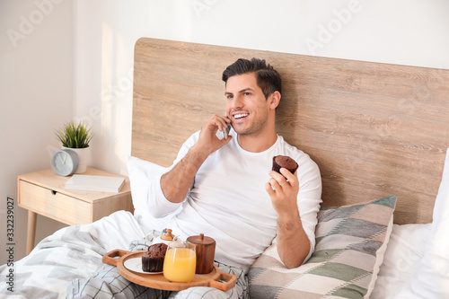 Morning of handsome young man talking by mobile phone during breakfast in bed