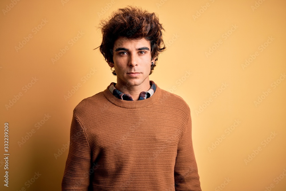 Young handsome man wearing casual shirt and sweater over isolated yellow background Relaxed with serious expression on face. Simple and natural looking at the camera. Young handsome man wearing casual shirt and sweater over isolated yellow background Relaxed with serious expression on face. Simple and natural looking at the camera.