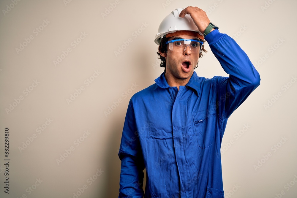 Fototapeta premium Young constructor man wearing uniform and security helmet over isolated white background surprised with hand on head for mistake, remember error. Forgot, bad memory concept.