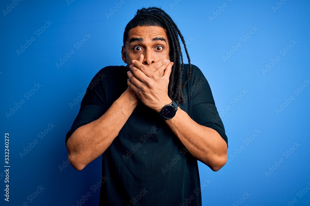 Young handsome african american afro man with dreadlocks wearing casual t-shirt shocked covering mouth with hands for mistake. Secret concept.