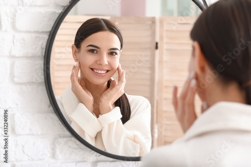 Beautiful young woman with healthy skin looking in mirror