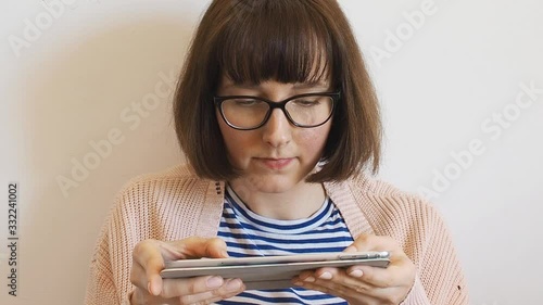 Young caucasian woman in spring pastel color clothes wearing black frame eyeglasses and using tablet at home