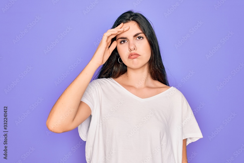 Young beautiful brunette woman wearing casual white t-shirt over purple background worried and stressed about a problem with hand on forehead, nervous and anxious for crisis
