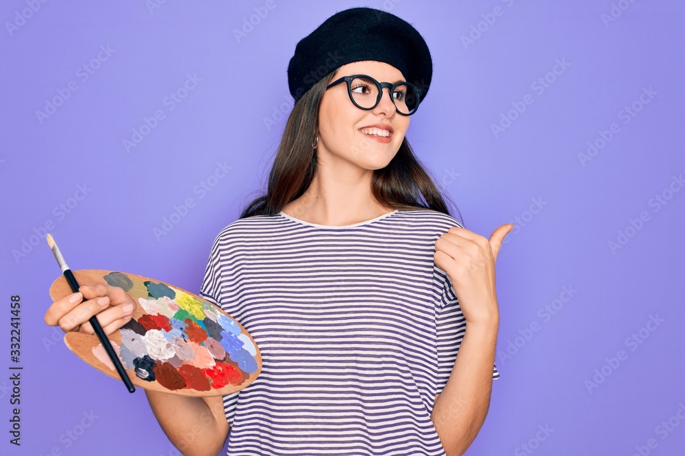 Young beautiful artist girl wearing fashion beret painting using paintbrush  and palette pointing and showing with thumb up to the side with happy face  smiling Photos | Adobe Stock