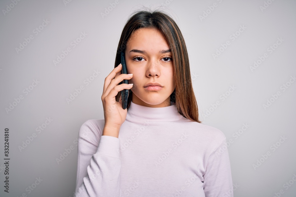 Beautiful brunette girl having conversation talking on the smartphone over white background with a confident expression on smart face thinking serious Beautiful brunette girl having conversation talking on the smartphone over white background with a confident expression on smart face thinking serious