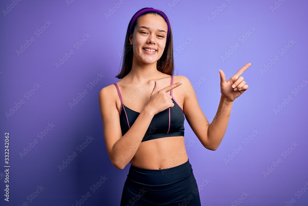 Young beautiful sporty girl doing sport wearing sportswear over isolated purple background smiling and looking at the camera pointing with two hands and fingers to the side. Young beautiful sporty girl doing sport wearing sportswear over isolated purple background smiling and looking at the camera pointing with two hands and fingers to the side.