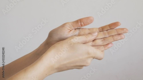 Beautiful female hands with nude manicure applying hand cream over gray wall