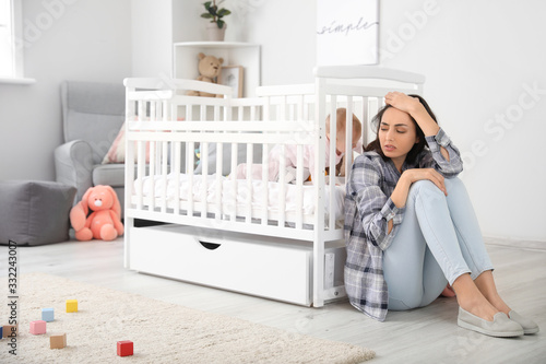 Young woman suffering from postnatal depression near bed with baby at home