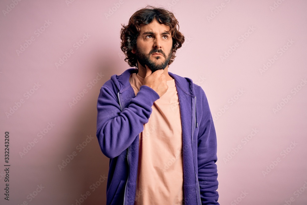 Young handsome sporty man with beard wearing casual sweatshirt over pink background Touching painful neck, sore throat for flu, clod and infection Young handsome sporty man with beard wearing casual sweatshirt over pink background Touching painful neck, sore throat for flu, clod and infection
