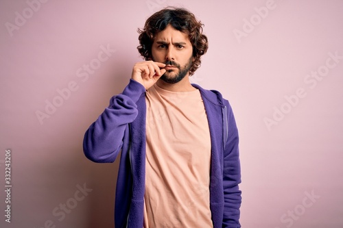 Young handsome sporty man with beard wearing casual sweatshirt over pink background mouth and lips shut as zip with fingers. Secret and silent, taboo talking