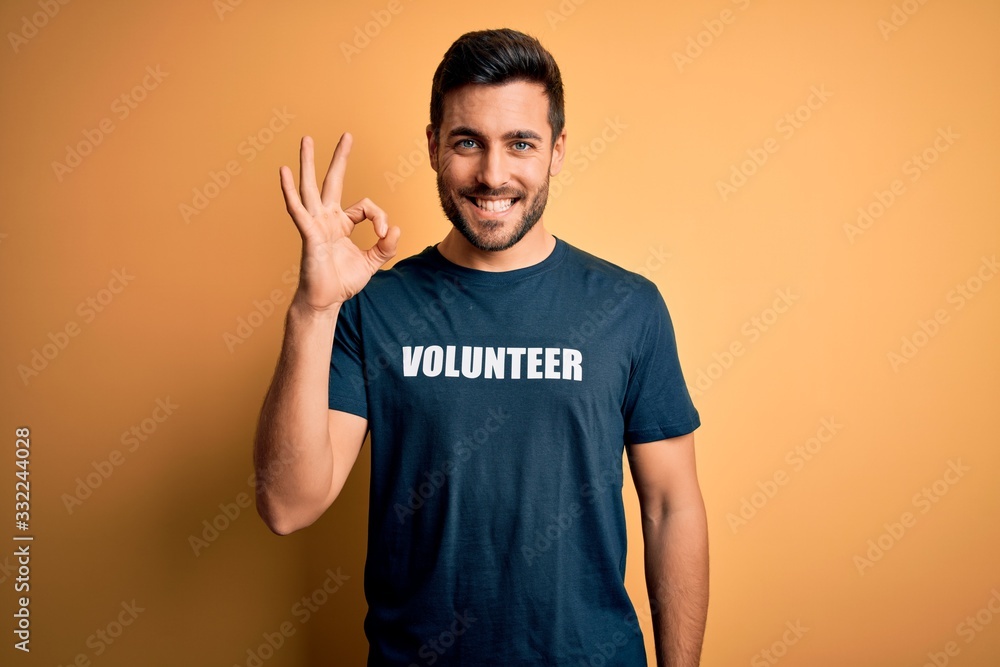 Young handsome man with beard volunteering wearing t-shirt with volunteer message doing ok sign with fingers, excellent symbol Young handsome man with beard volunteering wearing t-shirt with volunteer message doing ok sign with fingers, excellent symbol