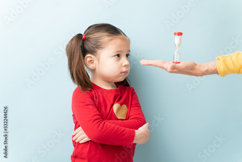 Hand of a parent holding a sand timer in front of a little girl while she is on timeout photo