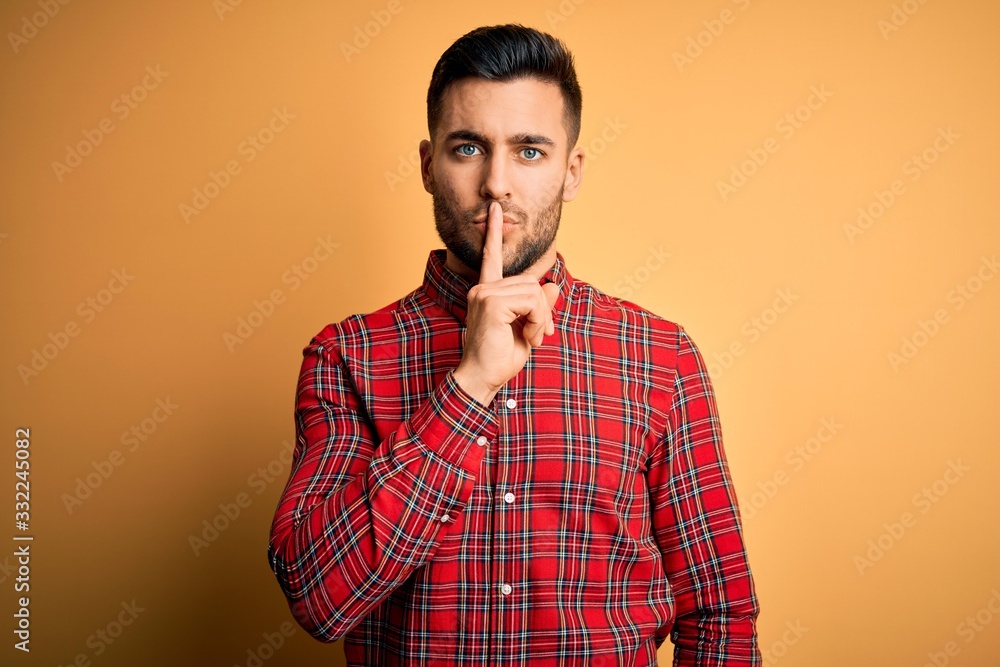 Young handsome man wearing casual shirt standing over isolated yellow background asking to be quiet with finger on lips. Silence and secret concept. Young handsome man wearing casual shirt standing over isolated yellow background asking to be quiet with finger on lips. Silence and secret concept.