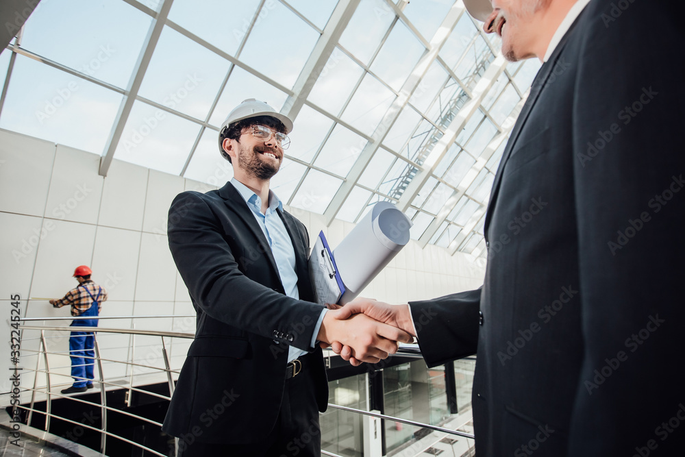 Two cheerful designers handshaking in helmet at new building. Two cheerful designers handshaking in helmet at new building.