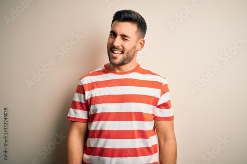 Young handsome man wearing casual striped t-shirt standing over isolated white background winking looking at the camera with sexy expression  cheerful and happy face.