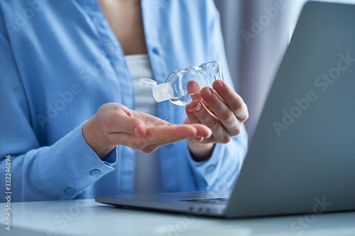 Woman uses an antibacterial antiseptic gel for disinfection and clean hands while working at a laptop. Hand protection against viruses, germs and bacteria during coronavirus outbreak