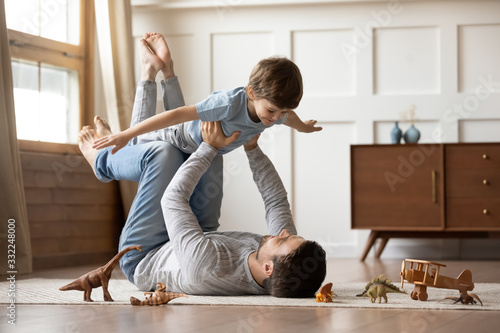 Happy young father lying on floor in living room hold fly with little preschooler son engaged in funny game together, loving dad relax playing with small boy child, enjoy family weekend at home photo