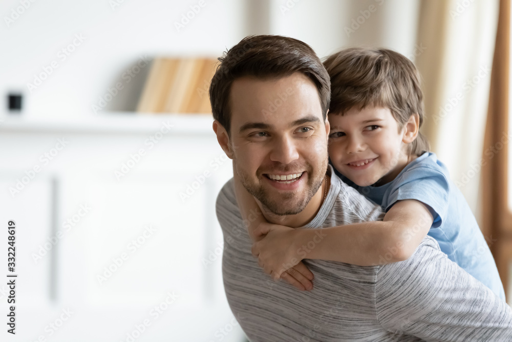 Smiling cute little boy piggyback young father playing together at home on weekend, happy father dad have fun carry on back engaged in funny game with small preschooler son, relaxing at home Smiling cute little boy piggyback young father playing together at home on weekend, happy father dad have fun carry on back engaged in funny game with small preschooler son, relaxing at home