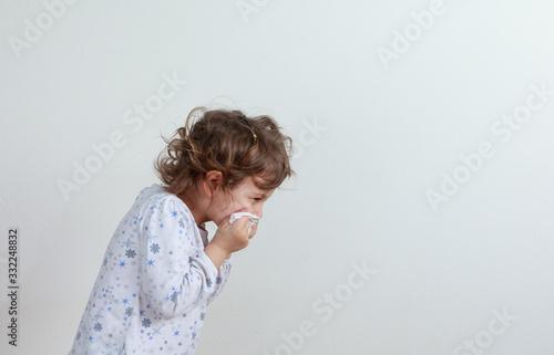 Young girl sneezing into a paper handkerchief, facing away, in front of a white background.