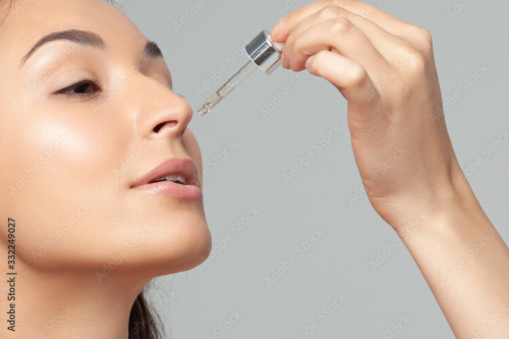 Young beautiful woman with clean perfect skin uses age-sensitive serum in pipette Young beautiful woman with clean perfect skin uses age-sensitive serum in pipette