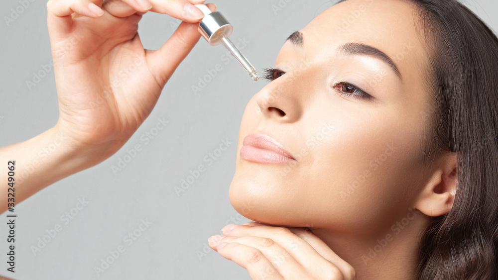 Young beautiful woman with clean perfect skin uses age-sensitive serum in pipette Young beautiful woman with clean perfect skin uses age-sensitive serum in pipette