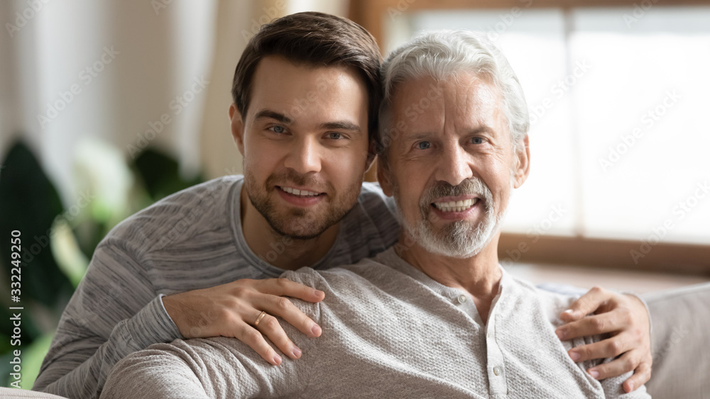 Portrait of smiling elderly father posing looking at camera hugging with adult grown-up son, happy young man embrace mature dad relax together at home on weekend, family value, relationships concept - obrazy, fototapety, plakaty 