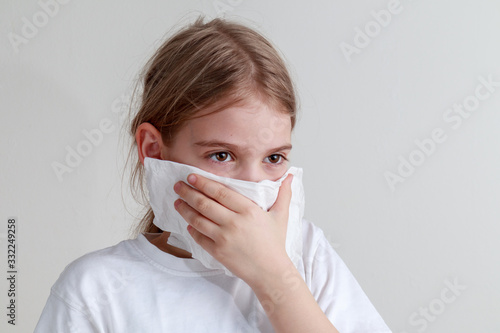 Young girl protecting herself with a paper handkerchief from germs and looking seriously in front of a white background.