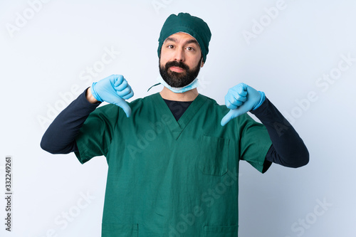 Surgeon man in green uniform over isolated background showing thumb down with two hands