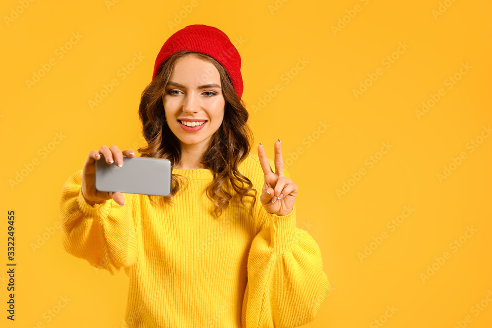 Young woman with mobile phone taking selfie on color background Young woman with mobile phone taking selfie on color background