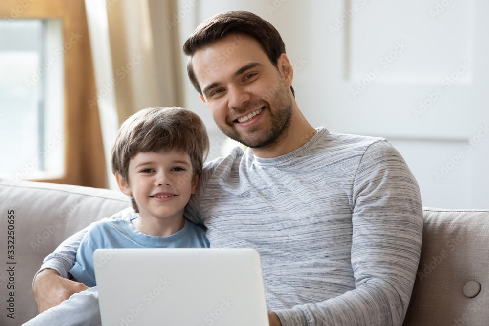 Portrait of smiling young father hug cuddle relax in living room with preschoolers son browsing computer, happy dad embrace little boy child rest on sofa at home using surfing laptop together Portrait of smiling young father hug cuddle relax in living room with preschoolers son browsing computer, happy dad embrace little boy child rest on sofa at home using surfing laptop together