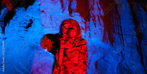 Man in chemical warfare suit and resperator mask aiming rifle  in a desert canyon sourounded by red and blue emergency lights photo