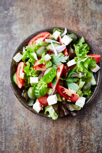 Healthy salad with feta cheese, green olives and tomatoes. Rustic stone background. Top view.