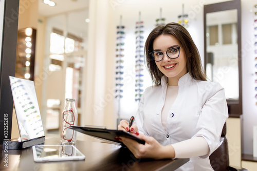 Medicine, pharmacy and optics. Portrait of young woman doctor or pharmacist in a white robe write a recipe in optical clinic © Тарас Нагирняк