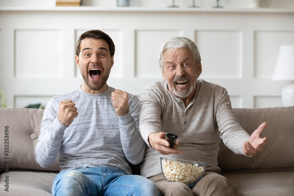 Senior father sit relax on couch with grown-up son watching sports game together, happy mature dad rest at home in living room with adult man child enjoying football match relaxing on weekend Senior father sit relax on couch with grown-up son watching sports game together, happy mature dad rest at home in living room with adult man child enjoying football match relaxing on weekend